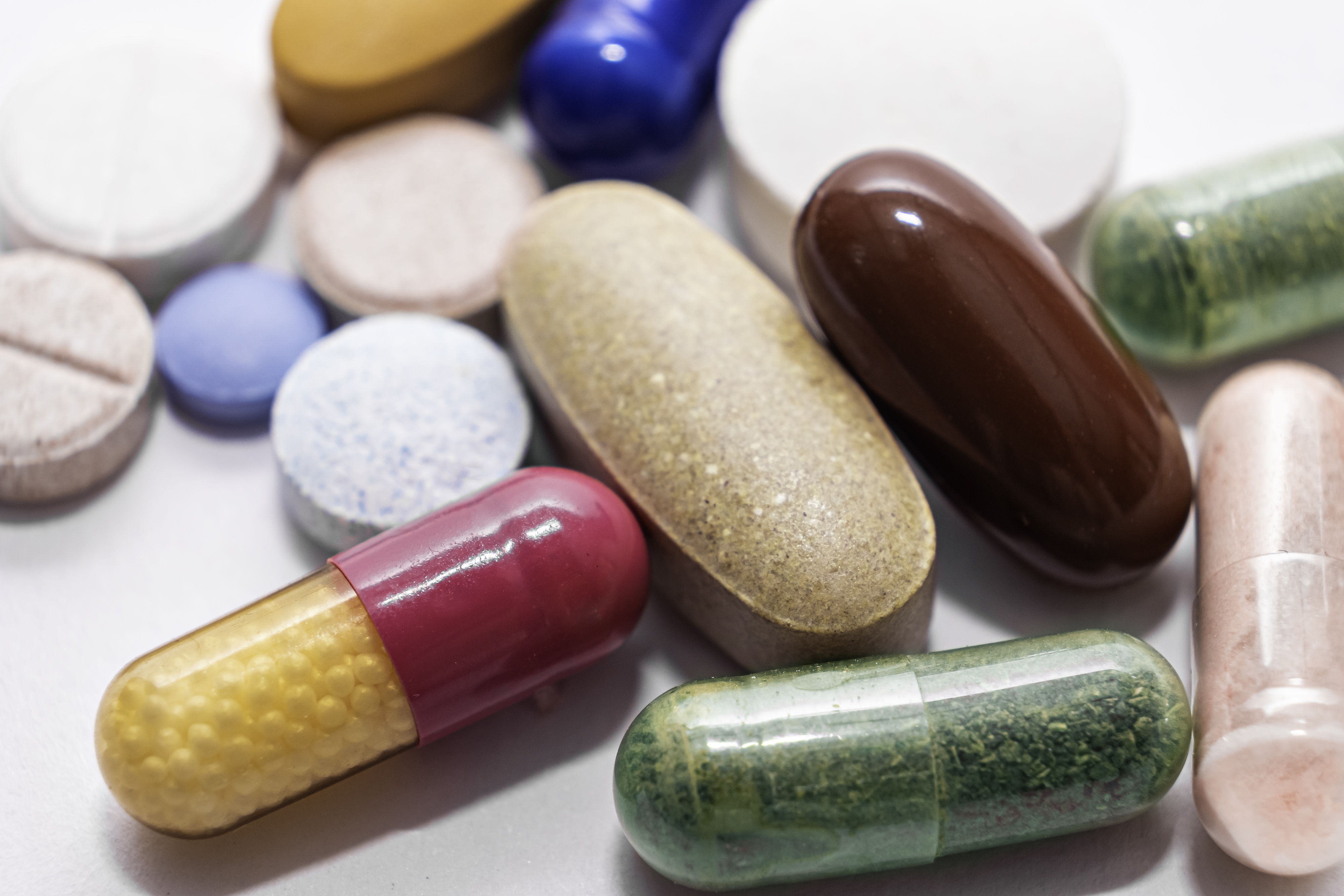 Close-up colorful powder soft capsules pill vitamin tablet blue pink yellow brown supplements on white background macro